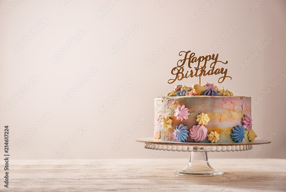 Stand with delicious birthday cake on table against light background