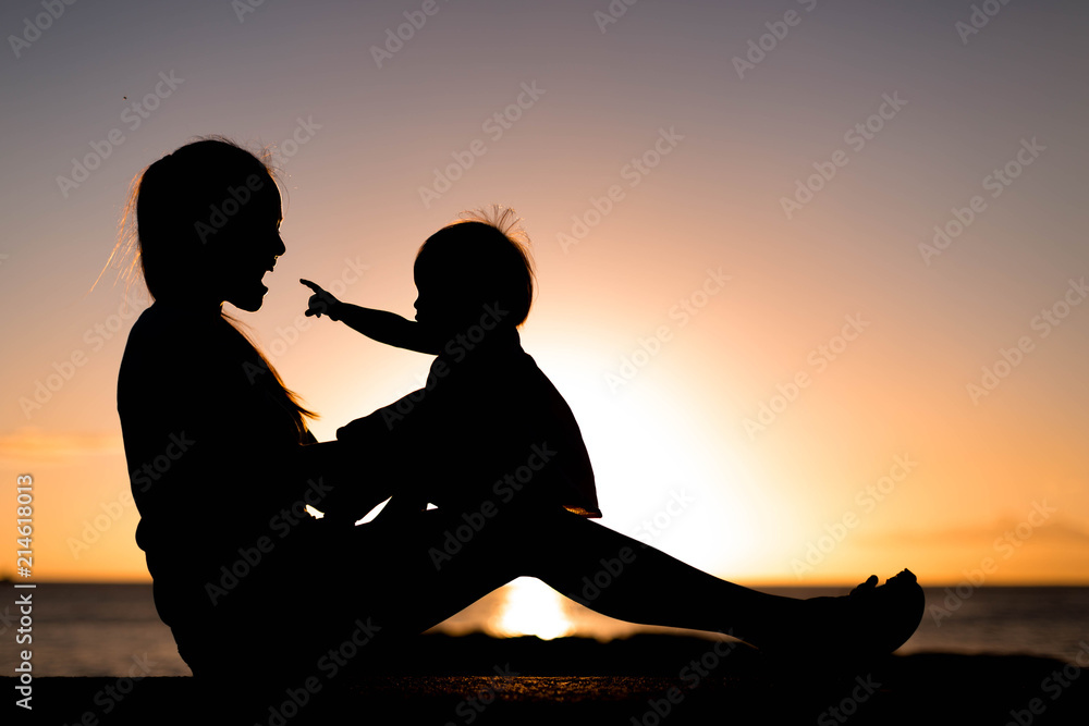 Mother and child playing and watching sunset on the beach in silhouette