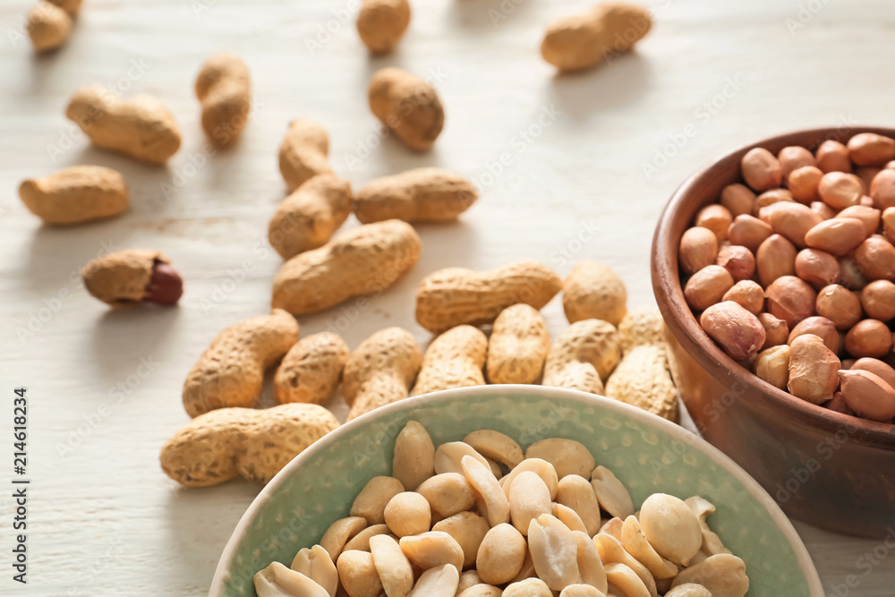 Bowls with tasty peanuts on white wooden background Bowls with tasty peanuts on white wooden background