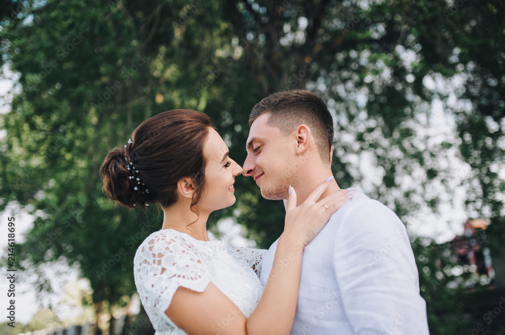 Beautiful newlyweds hugging against a background of green foliage. A stylish bridegroom gently presses a sweet bride. Wedding portrait close-up. Beautiful newlyweds hugging against a background of green foliage. A stylish bridegroom gently presses a sweet bride. Wedding portrait close-up.