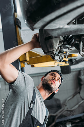 bottom view of workman in uniform repairing car in mechanic shop