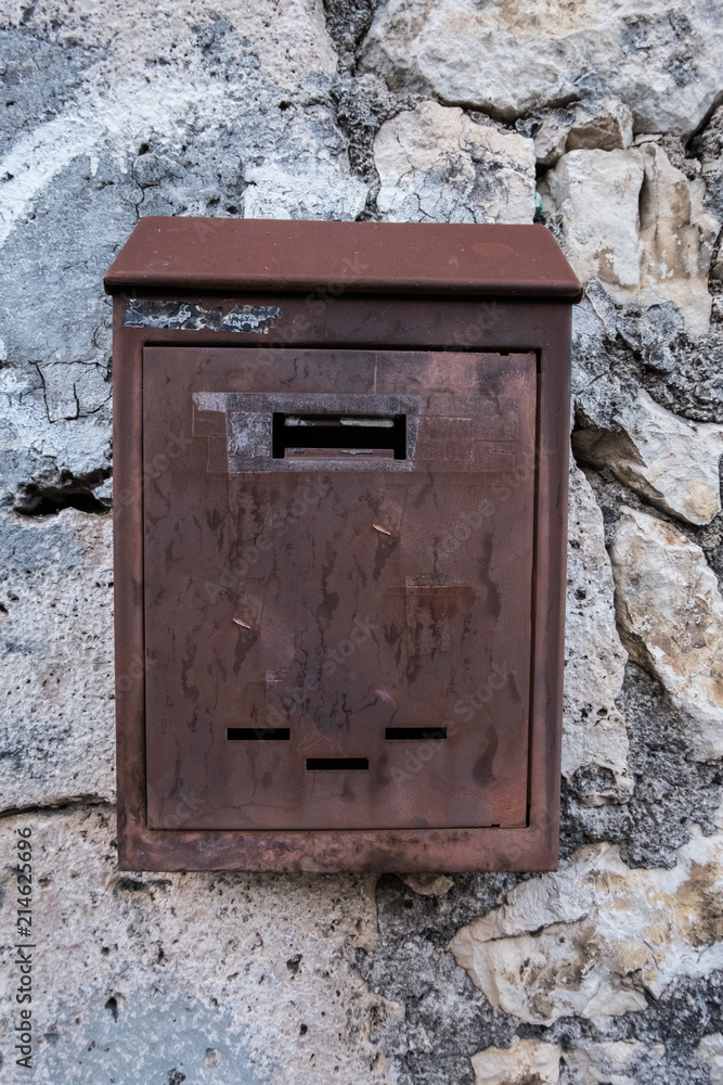 Vertical image of a mailbox with a wall in the background. No people.