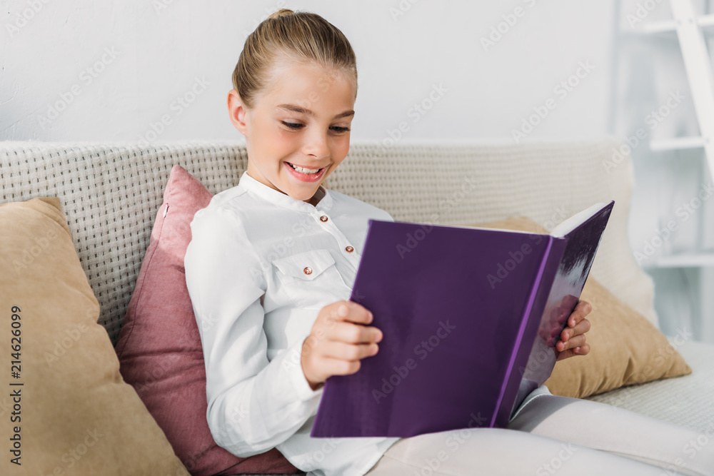 adorable little child reading book while relaxing on couch at home adorable little child reading book while relaxing on couch at home