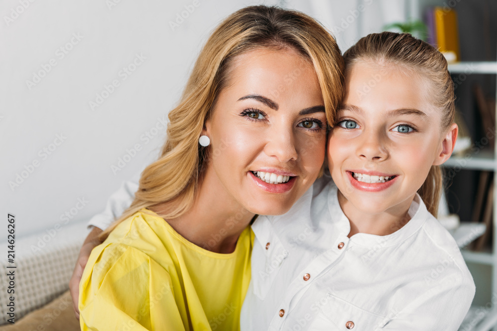 smiling mother and daughter sitting on couch and looking at camera smiling mother and daughter sitting on couch and looking at camera