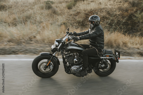 Man in black clothes riding a black classic American motorcycle in a road.