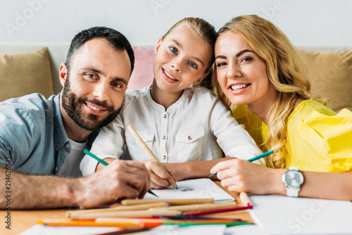happy young family drawing with color pencils together and looking at camera