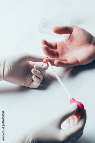 cropped shot of doctor taking blood of patient for test on white tabletop
