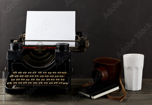 Vintage typewriter with empty, blank sheet of paper, camera, cup and notebook on wood table