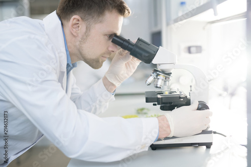 Side view portrait of scientist looking in microscope while doing research in medical laboratory