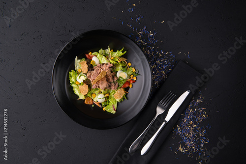 a dish of boiled meat on a black wooden surface, top view