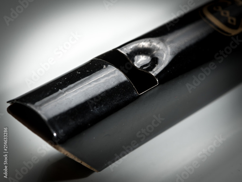 A black tin whistle lying on a white reflective surface photo