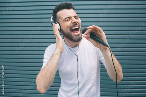 Happy musician is enjoying listening to music. He wears headphones and singing. Guy is using karaoke. Man is singing ot loud. Isolated on striped and blue background. photo