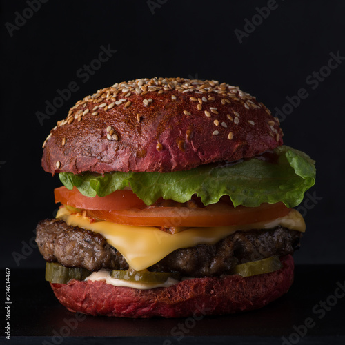 juicy  cheeseburger of red bread on a black background, close-up