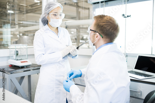 Portrait of two modern young scientists wearing lab coats discussing project while working in medical laboratory