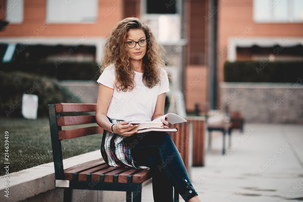 Female student sitting in a campus and waiting for class to begin. Books in hands. Female student sitting in a campus and waiting for class to begin. Books in hands.