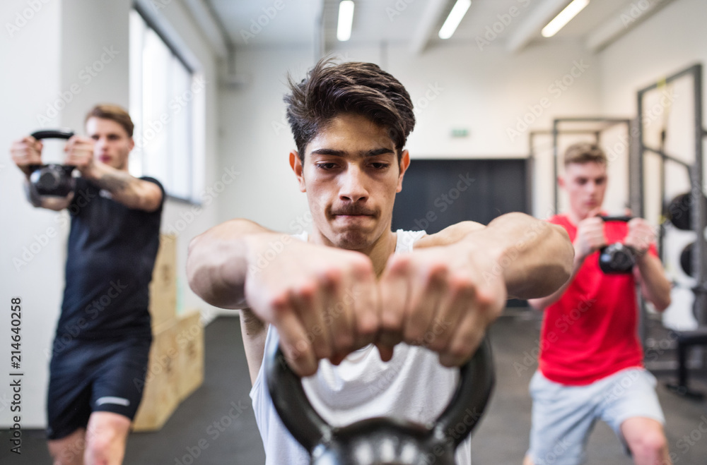 Naklejka premium Three young men in gym doing kettlebell swings.