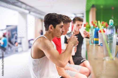 Men in gym sitting and holding glasses of protein drink.