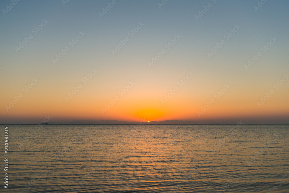 sunrise at sea with cargo ship on horizon