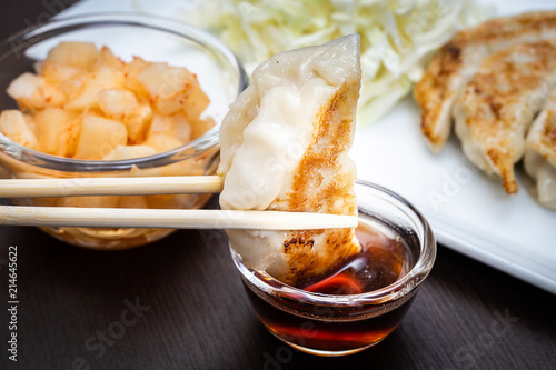 hand with chopsticks holding a piece of gyoza fried - dumplings snack , with soy sauce