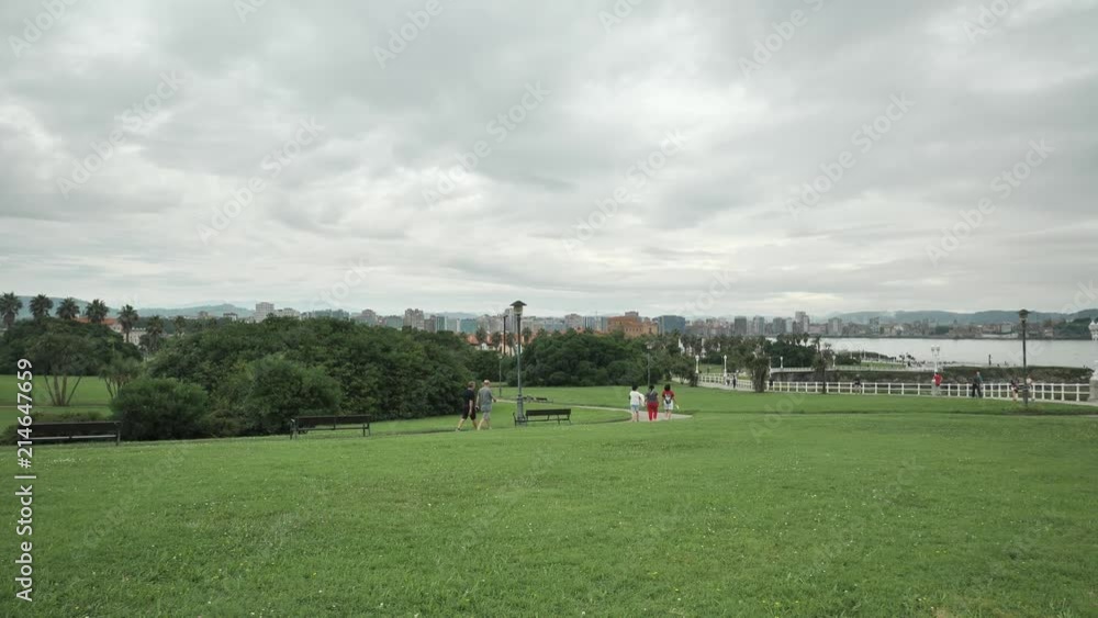 Green city park overview with a plenty of green plants and tries of different types, wlaking people and city buildings on it´s back Green city park overview with a plenty of green plants and tries of different types, wlaking people and city buildings on it´s back