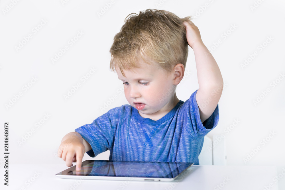 Three years old little kid boy playing children educational or developing games or on the tablet computer at home on white background Three years old little kid boy playing children educational or developing games or on the tablet computer at home on white background