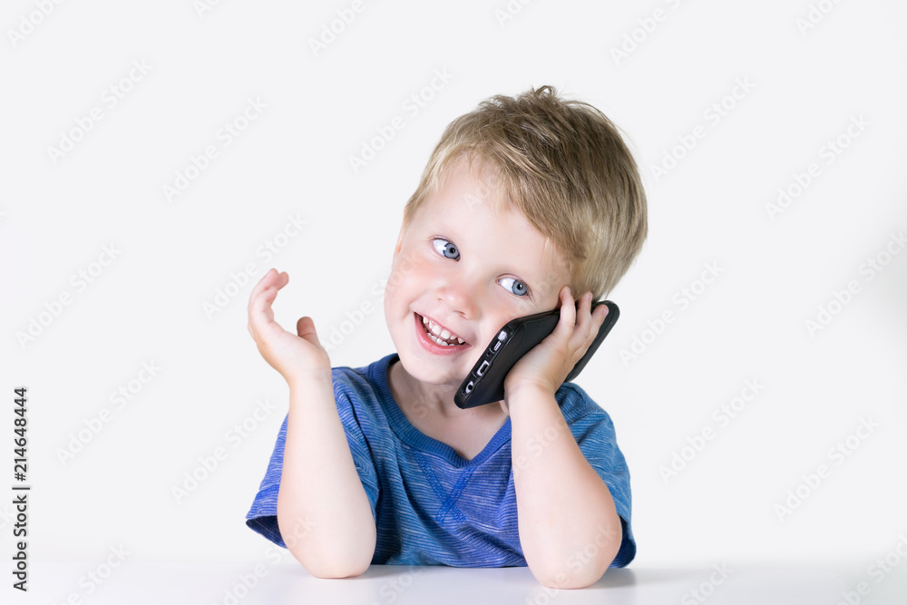 Little kid boy with mobile phone in hands, looking in it and talking on white background. Children and smartphone, new technology concept Little kid boy with mobile phone in hands, looking in it and talking on white background. Children and smartphone, new technology concept