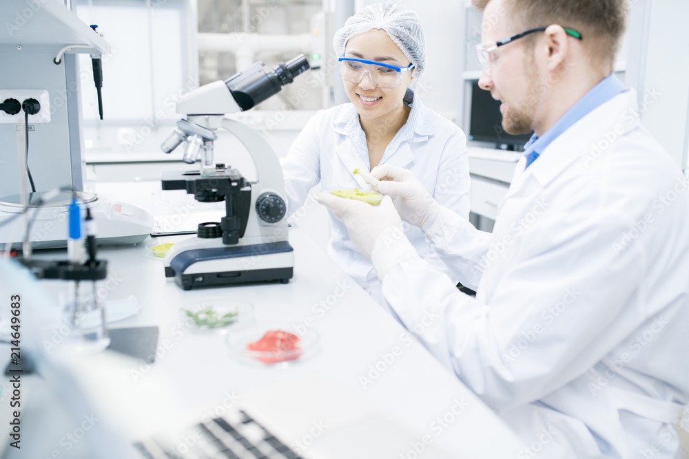 Portrait of two modern young scientists smiling while doing research studying food substances in laboratory, copy space Portrait of two modern young scientists smiling while doing research studying food substances in laboratory, copy space