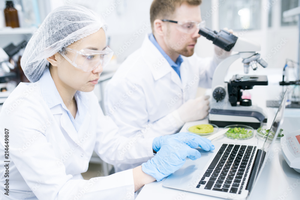 Portrait of two modern young scientists doing research studying substances in laboratory and using laptop, copy space Portrait of two modern young scientists doing research studying substances in laboratory and using laptop, copy space