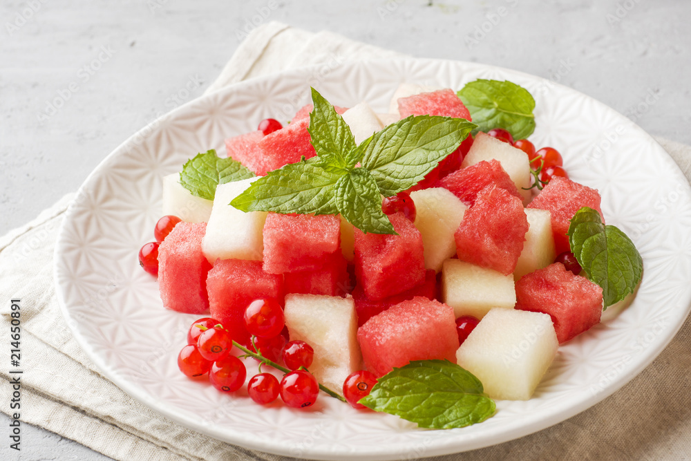 Salad of fresh juicy pieces of watermelon, melon, red currant and mint leaves on a plate. Salad of fresh juicy pieces of watermelon, melon, red currant and mint leaves on a plate.