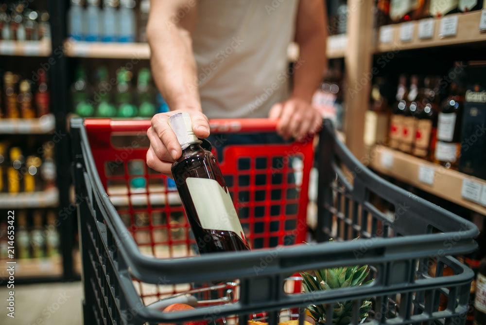 Male person put bottle of wine in a cart
