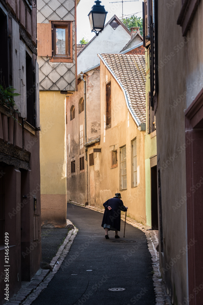 An old lady struggles up the street in the picturesque village of Ribeauville, France An old lady struggles up the street in the picturesque village of Ribeauville, France