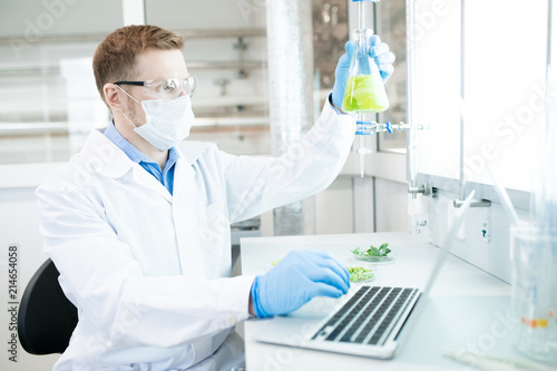 Side view portrait of modern scientists working on medical research studying liquids in beaker while sitting at table in laboratory