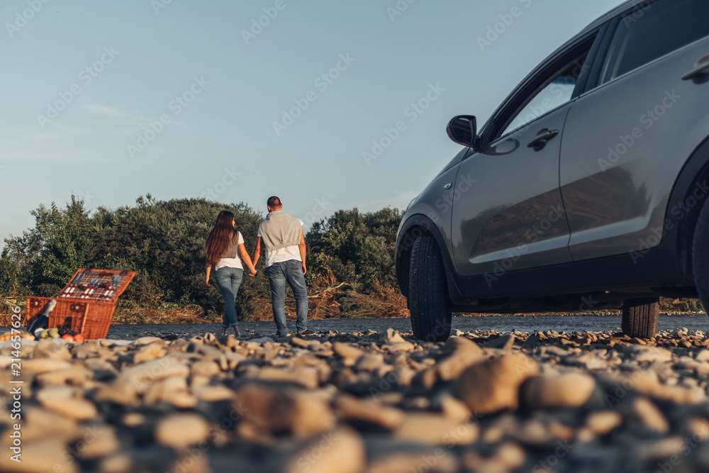 Happy Traveler Couple on Picnic into the Sunset with SUV Car - obrazy, fototapety, plakaty 