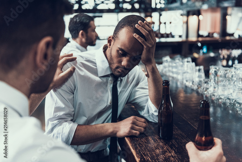 Young Man Supporting Sad Friend in Modern Bar.