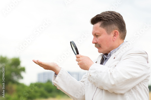 Adult middle aged man with a mustache looks through a magnifying glass.