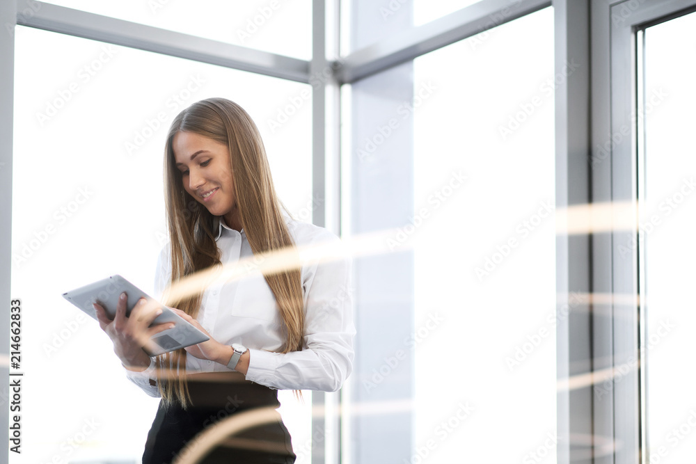 Young beautiful girl uses tablet in office with glass walls. Young beautiful girl uses tablet in office with glass walls.