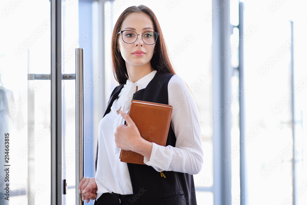 A young beautiful girl in eyeglasses enters glass office door.