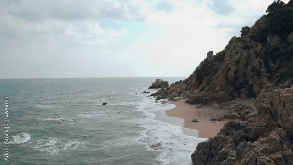 Aerial side view of the ocean waves hitting the sandy beach below the cliff in the Mediteranean sea Aerial side view of the ocean waves hitting the sandy beach below the cliff in the Mediteranean sea
