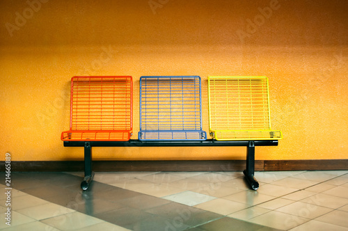 Multicolored metal seats stand at the marine station on the background of an orange wall. The concept of waiting time. photo