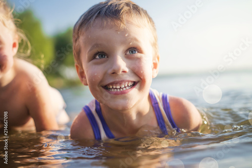 Obraz na płótnie Portrait of beautiful children laugh and bathe in the sea. boy smiles and swims in lake. Good mood kids on summer lake. w salonie