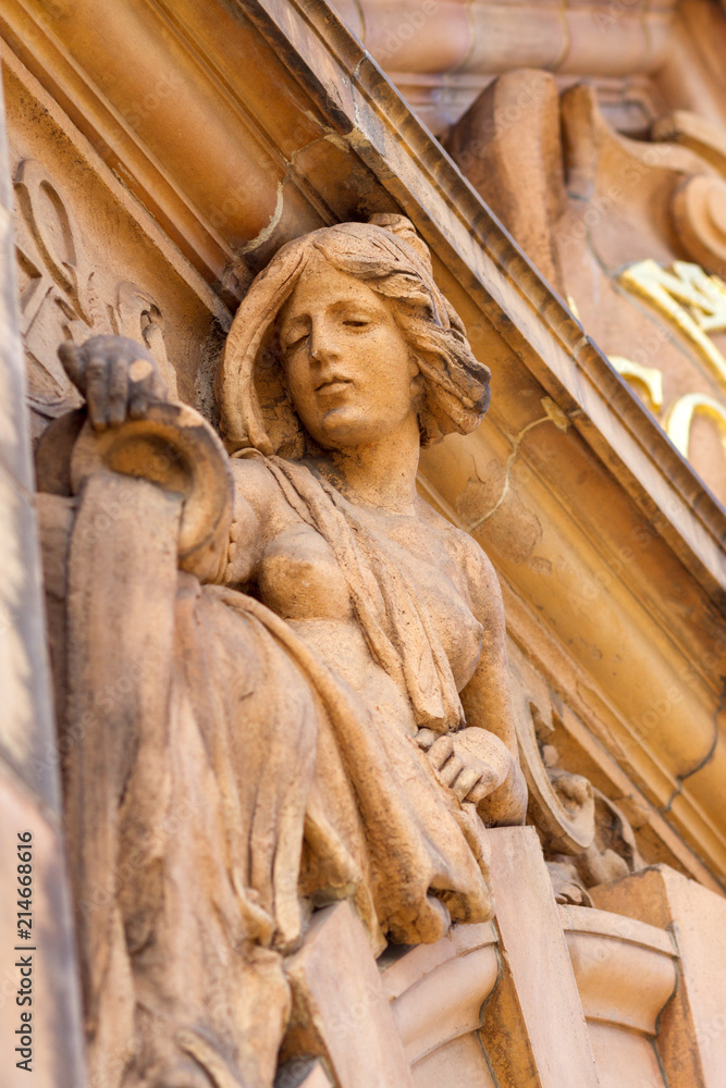 Seen from below the carved statue of a woman pouring water on the outside of a building in London