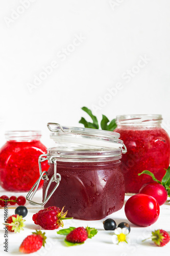 assortment of jams, seasonal fresh berries and fruits on white background