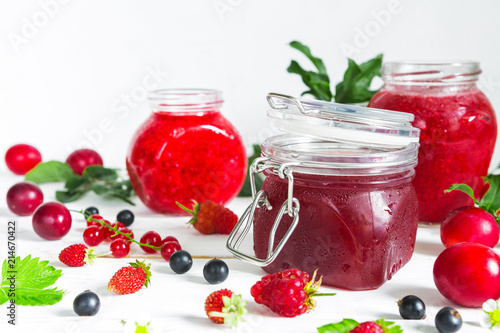 assortment of jams, seasonal fresh berries and fruits on white background