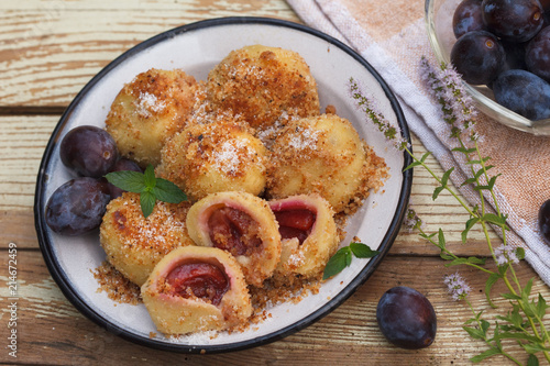 Typical Austrian plum dumplings made of leavened dough and fresh plums. Vintage wooden background decorated with mint flowers.