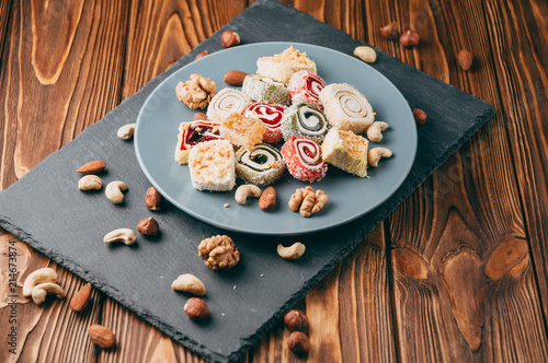 Traditional oriental sweets and nuts: hazelnuts, cashews on a brown wooden background. Turkish dessert is the locus of Rahat. View from above. Place under the text. photo