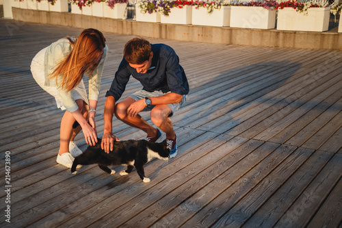 Young couple playing with a cat outside at the beach at the wooden deck summer time