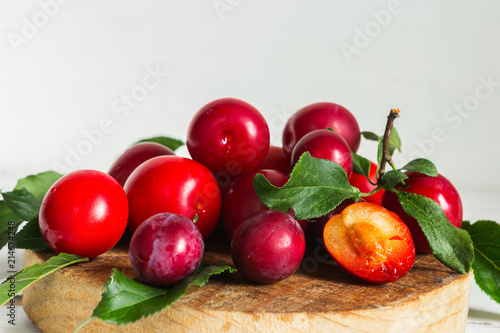 Fresh red plum with leaves on a wooden light background