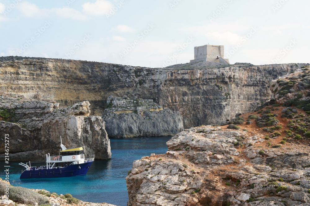 Boat on the lagoon with high cliffs and Santa Marija Tower on Comino Island in Malta (Torri ta' Kemmuna)