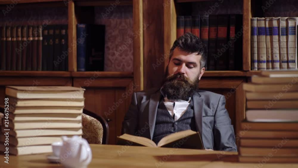 A bearded man stocked with books in a library reads a book. Library Concept. The professor prepares for a lecture in the library. A bearded man stocked with books in a library reads a book. Library Concept. The professor prepares for a lecture in the library.