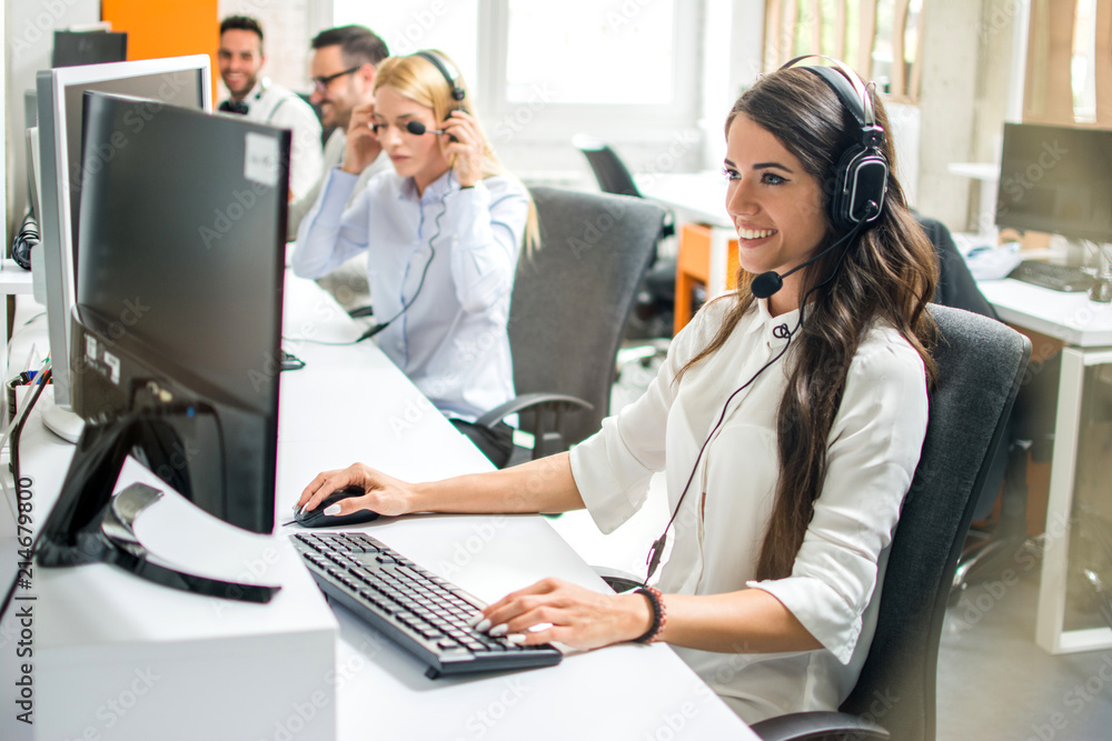 Young employee working with a headset accompanied by her team in call center Young employee working with a headset accompanied by her team in call center